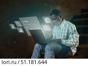 Young man using laptop while interacting with digital projections of charts and calendars in a cozy indoor setting. Стоковое фото, фотограф Сергей Толмачёв / Фотобанк Лори