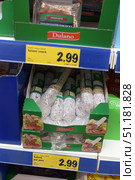 Supermarket shelves with Dulano brand salami sausages. The product is packaged in transparent film, showing the white casing and dense texture of the sausage. The sausages are placed in green cardboard trays with the Dulano brand name and an image of a serving with salami and vegetables. The price tags indicate the cost - 2.99 euros for 250 g (11.96 euros per kilogram). The top shelf also contains Dulano products, in particular, sliced ​​​​meats. A bright yellow price board emphasizes the promotional design, typical of chain stores. The photo demonstrates the product design, packaging and prices in the sales area. (2015 год). Редакционное фото, фотограф Анна Кривицкая / Фотобанк Лори