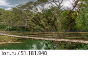 A rickety Bamboo Hanging Bridge over a tropical river. A wicker path, an unreliable railing. Green vegetation on the shore. Clouds in the sky. Philippines. Bohol. Sipatan River. Sevilla (2024 год). Стоковое фото, фотограф Вера Ивановна Кубарева / Фотобанк Лори