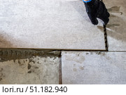 A worker lays gray ceramic tiles during a floor renovation, ensuring precise alignment with plastic spacers. Стоковое фото, фотограф Коханова Наталья / Фотобанк Лори