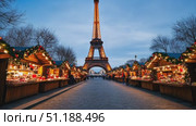 Festive Christmas market in Paris with wooden stalls decorated with garlands and glowing lights, leading up to the illuminated Eiffel Tower at twilight. This cozy winter holiday atmosphere reflects the joy of the New Year and Christmas season in France. Стоковое AI-видео, аниматор Ксения Чунаева / Фотобанк Лори