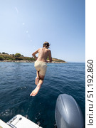 Boy plunging gleefully from boat stern into sparkling turquoise Aegean waters during sunny Greek island summer holiday. Стоковое фото, фотограф Данил Руденко / Фотобанк Лори