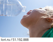 Child sipping bottled water, refreshing moment against bright summer sky. Стоковое фото, фотограф Данил Руденко / Фотобанк Лори