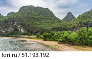 Lush green vegetation grows on the pebbly riverbank. Picturesque coastal mountains against the sky and clouds. China. Li River. Li Jiang. Guilin. Стоковое фото, фотограф Вера Ивановна Кубарева / Фотобанк Лори