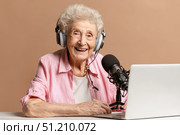 Elderly caucasian woman podcasting with microphone and laptop in studio setting. Стоковое AI-изображение, AI-художник Евгения Пархоменко / Фотобанк Лори
