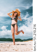 Young girl in bikini and straw hat posing playfully on sandy beach under blue sky. Concept of summer fashion, beach lifestyle, holiday vibes, and freedom mood. Стоковое фото, фотограф Енваев Андрей / Фотобанк Лори
