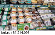 Supermarket shelf with a large assortment of ready-made meals in packages. In the foreground are products under the Lenta Fresh, Natur Buffet and PAN brands. In plastic containers and round portion boxes you can see a variety of dishes: meatballs with mashed potatoes, udon noodles with vegetables and chicken, set lunches, cutlets and other options. The packages are neatly laid out in rows, with price tags and promotional offers visible at the top. At the bottom of the frame is a sign advertising a combo set - soup plus a main course. The atmosphere of the photo emphasizes the convenience and variety of ready-made meals for a quick lunch or dinner. Редакционное фото, фотограф Анна Кривицкая / Фотобанк Лори