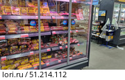 A refrigerated shelf of a supermarket with a variety of sausage products. On the shelves in vacuum packaging are laid out boiled, semi-smoked and dry-cured sausages, frankfurters and wieners of different brands. The most frequently highlighted products are those in yellow packaging of the Papa Mozhet brand - creamy, juicy and fried sausages. Also visible are loaves of salami and cervelat sausage. The prices for the products are indicated on the price tags under each shelf. The photo conveys the atmosphere of a grocery store, focusing on the assortment of meat products. Редакционное фото, фотограф Анна Кривицкая / Фотобанк Лори