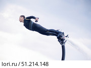 The man in a wetsuit seems to be flying like a superhero in the air against the background of the sky above the water, he is an athlete and a pilot of a hydroflight or a flyboard. Стоковое фото, фотограф Владимир Разгуляев / Фотобанк Лори
