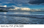 Early morning. The ocean waves roll towards the shore, foam, and spread out. The silhouette of a man in the water. The clouds in the blue sky are highlighted in gold. Malaysia. Borneo. Kota Kinabalu. Стоковое фото, фотограф Вера Ивановна Кубарева / Фотобанк Лори