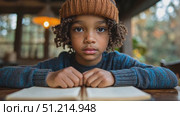 A young child sits patiently at a wooden table, gazing thoughtfully at an open notebook in a warm, rustic room on a cool day. Стоковое AI-видео, аниматор Данила Большаков / Фотобанк Лори