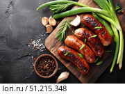 Fried Sausages on a wooden board with green onions and spices against a dark background, top view. Served on a black marble stone table. Grilled sausages. Delicious food advertising, banner design. Стоковое AI-изображение, AI-художник Марина Демидюк / Фотобанк Лори