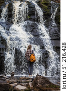 Tourism. Hiking. A young woman with a backpack on her back stands in front of the Yukankoski Waterfall (White Bridges) in the Republic of Karelia. Стоковое фото, фотограф Photojuli / Фотобанк Лори