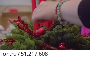 A woman decorates her home for the holidays by creating a festive wreath using fir branches and festive ornaments. Стоковое видео, видеограф Strunov David / Фотобанк Лори