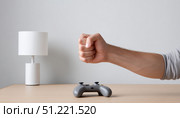 Frustrated gamer clenching fist near gamepad, displaying intense emotion after losing competitive video game, dimly lit home gaming workspace visible. Стоковое AI-изображение, AI-художник Юрий Поздников / Фотобанк Лори