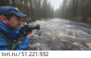 Professional photographer documenting wild river dynamics in boreal forest, wearing waterproof gear near rushing stream during overcast weather conditions. Стоковое AI-видео, аниматор Юрий Поздников / Фотобанк Лори