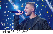 Dynamic vocalist performing onstage, wearing black attire, gripping microphone while golden confetti cascading during high energy musical concert. Стоковое AI-видео, аниматор Юрий Поздников / Фотобанк Лори
