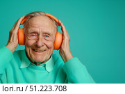 Улыбающийся пожилой мужчина в оранжевых наушниках слушает музыку на бирюзовом фоне. Стоковое AI-изображение, AI-художник Кирилл Сиротюк / Фотобанк Лори