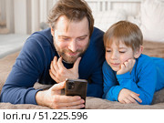 Father and son little boy laughing and using phone. They watching funny videos together, playing games on smartphone. Concept technology, smart phone addicted. Fun weekend activity. Modern fatherhood. Стоковое фото, фотограф Марина Демидюк / Фотобанк Лори