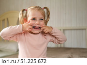 Little Girl joking sticking tongue out with silly expression. Child making face. Funny foolishness portrait of baby girl laughing in bedroom. Adorable Caucasian kid doing crazy comical gesture at home. Стоковое фото, фотограф Марина Демидюк / Фотобанк Лори