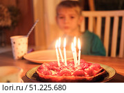 Little happy boy blows out candles on birthday cake and makes a wish. Child celebrates party at home with a sweet cake and flickering candles in a warm setting. Birthday Celebration, joyful moments. Стоковое фото, фотограф Марина Демидюк / Фотобанк Лори