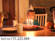 Little happy boy blows out candles on birthday cake and makes a wish. Child celebrates party at home with a sweet cake and flickering candles in a warm setting. Birthday Celebration, joyful moments. Стоковое фото, фотограф Марина Демидюк / Фотобанк Лори