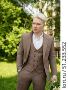 Young man in tailored suit standing confidently in a green park setting. Стоковое фото, фотограф Гурьянов Андрей / Фотобанк Лори