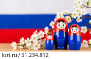Три ярко разукрашенные русские матрешки на фоне российского флага и белых яблонь в цвету. Three brightly decorated Russian nesting dolls on the background of the Russian flag and white apple trees in bloom. Стоковое AI-изображение, AI-художник ketpro.design / Фотобанк Лори