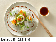 Cellophane noodles. White plate of salad with Glass Noodle and colorful vegetables, vibrant colors. Wooden chopsticks beside it, and orange sauce on top. Light beige background. Warm Asian salad. Стоковое AI-изображение, AI-художник Марина Демидюк / Фотобанк Лори