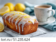 Homemade lemon drizzle cake with icing. Classic lemon pound cake with citrus glaze and zest. Whole loaf, side view, close up. Fresh homemade baked dessert with lemon slices. Blurred tea set background. Стоковое AI-изображение, AI-художник Марина Демидюк / Фотобанк Лори