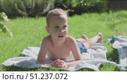 A Young Boy is Relaxing on His Towel in the Bright, Sunlit Grass of a Beautiful Day. Стоковое видео, видеограф Olesia Kondrateva / Фотобанк Лори