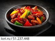 Sweet sour pork with colorful peppers, mixed vegetables served in a black bowl on dark concrete background. Traditional Chinese dish. Close-up. The meat pieces in a brown sauce glaze. Sichuan cuisine. Стоковое AI-изображение, AI-художник Марина Демидюк / Фотобанк Лори