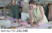 Young seamstress cutting fabric with scissors in a sewing workshop. Стоковое видео, видеограф Яков Филимонов / Фотобанк Лори