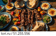 Delicious grilled lamb kofta kebabs served with pita bread, hummus, and salad on wooden table. Стоковое фото, фотограф David Kashakhi / Фотобанк Лори
