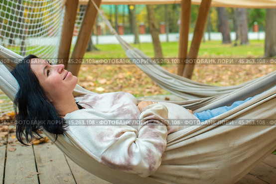42-летняя беременная женщина отдыхает, лежа в гамаке в осеннем парке. беременность после 40, 8 месяцев, 3 триместр. Стоковое фото, фотограф Яна Проничева / Фотобанк Лори