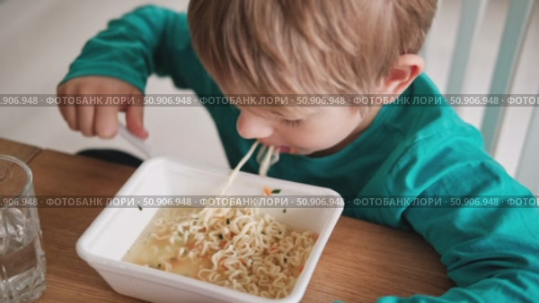 6 years old boy eats instant noodle from box. Child is eating spaghetti. Lunch time. A good appetite. Tasty children food. Close-up portrait. Carbs dinner. Fast food. Kid eating by himself with fork. Стоковое видео, видеограф Марина Демидюк / Фотобанк Лори