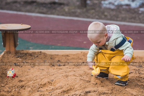 A beautiful, cheerful little boy of two years old walks on the playground in the spring. A child is playing with a shovel in the sandbox. The concept of parenthood, happy childhood and family. Стоковое фото, фотограф Photojuli / Фотобанк Лори