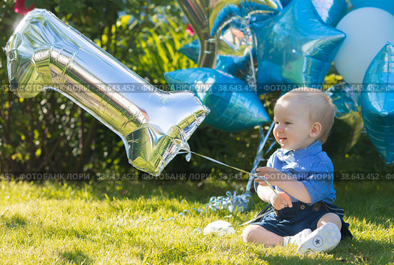 A beautiful little boy kid gentleman in a retro suit with suspenders and a bow tie is sitting on a green lawn. Children's party with balloons happy birthday, 1 year. Стоковое фото, фотограф Photojuli / Фотобанк Лори