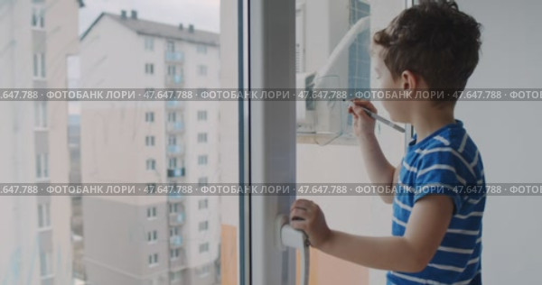 A boy draws on a window, showing creativity and curiosity about the world. Стоковое видео, видеограф Cantemir Dumitru / Фотобанк Лори