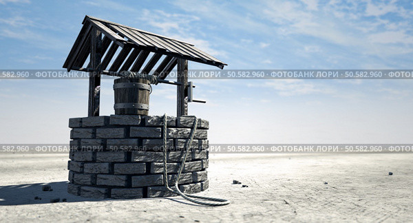 A brick water well with a wooden roof and bucket attached to a rope in a flat barren landscape with a blue sky background. Стоковое фото, агентство Ingram Publishing / Фотобанк Лори