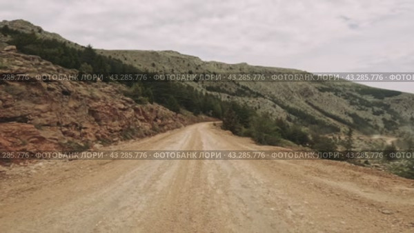 A bumpy dirt road winds through a forested landscape, framed by majestic mountains in the distance. Стоковое видео, видеограф ILIA GOROKHOV / Фотобанк Лори