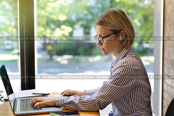 A businesswoman in glasses works on a laptop near the window. Стоковое фото, фотограф Alexandra Aleroewa / Фотобанк Лори