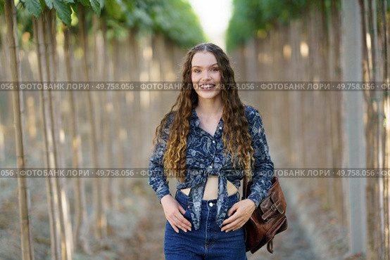 A cheerful and vibrant young woman is joyfully posing in a picturesque vineyard, showcasing her stylish and fashionable outfit amidst the beautiful and lush rows of grapevines that surround her. A Young Woman Smiling Happily in a Vineyard Surrounded by Beautiful Lush Green Rows. Стоковое фото, агентство Ingram Publishing / Фотобанк Лори