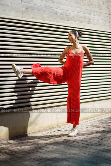 A cheerful and vibrant young woman showcases her bold red attire while playfully posing against a beautifully textured wall, perfectly combining elements of fashion and fun in her dynamic expression. A Joyful Young Woman is Posing with a Stylish Red Outfit Against a Contemporary Modern Wall. Стоковое фото, агентство Ingram Publishing / Фотобанк Лори