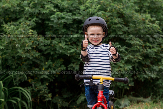 A cheerful little boy rides a running bike in a helmet outdoors. A happy child is engaged in an active sport. Protection. Life insurance and child safety. Стоковое фото, фотограф Photojuli / Фотобанк Лори