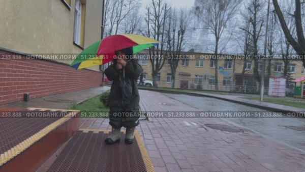 A child is joyfully playing with a colorful umbrella during a rainy weather, enjoying the moment. Стоковое видео, видеограф Olesia Kondrateva / Фотобанк Лори