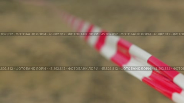 A close-up of a red and white striped tape, used for marking off areas, stretches into the blurred background. Usually such tape is used to cordon off areas. The wind ruffles the red and white ribbon. Стоковое видео, видеограф Воловодов Владимир / Фотобанк Лори