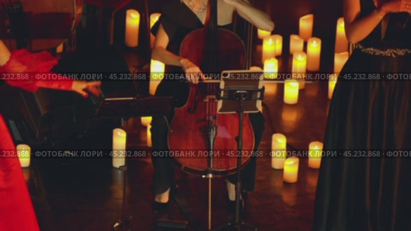 A close-up of a woman playing the cello. A group of women performing music on a dimly lit stage illuminated by numerous candles. They are all dressed in evening gowns. Стоковое видео, видеограф Воловодов Владимир / Фотобанк Лори