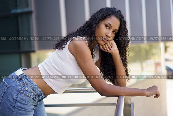 A confident young woman elegantly poses in a casual manner against a stylish railing in an urban environment, effortlessly showcasing her exceptional fashion sense and her natural beauty. A Stylish Young Woman is Posing Outdoors in a Vibrant Urban Environment with Confidence and Grace. Стоковое фото, агентство Ingram Publishing / Фотобанк Лори