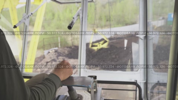 A crane operator skillfully maneuvers the controls from the cabin, overseeing the loading of coal into a barge for northern delivery along the Yenisei river. View of a young male crane operator at work controlling a joystick in the crane cabin rear view, working professions. Стоковое видео, видеограф Владимир Разгуляев / Фотобанк Лори